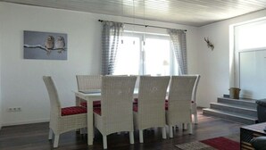Uma sala de jantar com cadeiras de vime, uma mesa branca e uma janela com cortinas.