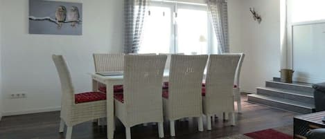 Un coin repas avec des chaises en osier, une table blanche et une fenêtre avec des rideaux.