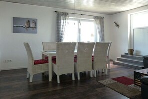 A dining area with wicker chairs, a white table, and a window with curtains. - City view Winterberg (Winterberg)
