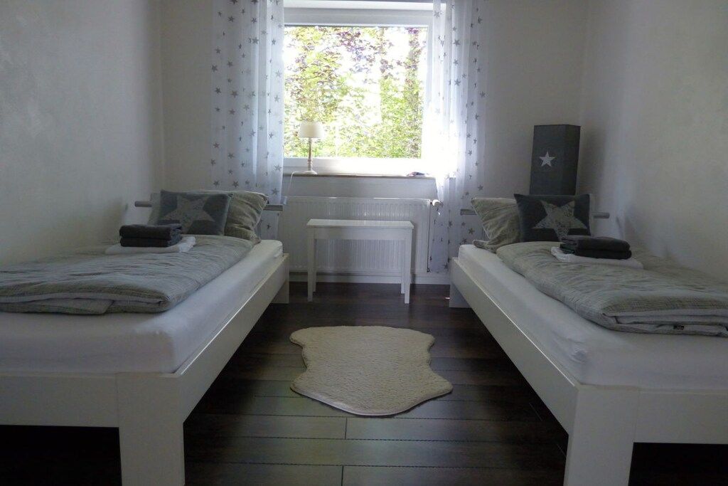 A room with two beds, a radiator, a window with curtains, and a star-shaped decoration on the wall.