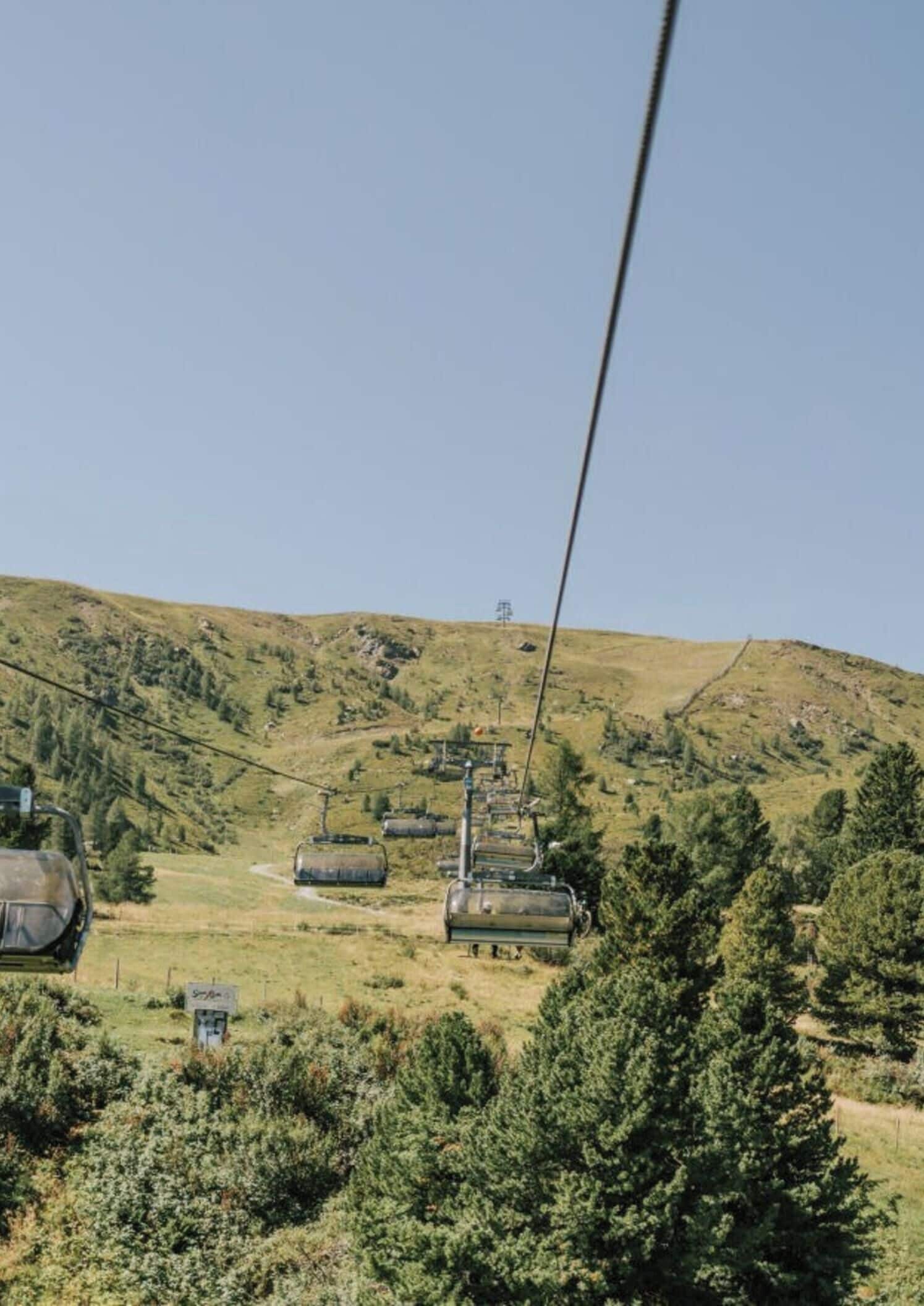 A cable car system in a mountainous area with green vegetation and clear skies.