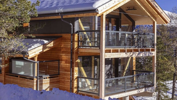 Uma cabana de madeira com varanda de vidro, rodeada por neve.