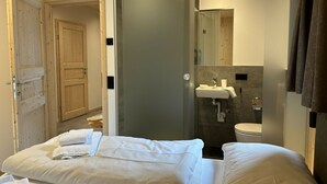 Quarto de hotel com cama, banheiro com pia e vaso sanitário, e porta de madeira.