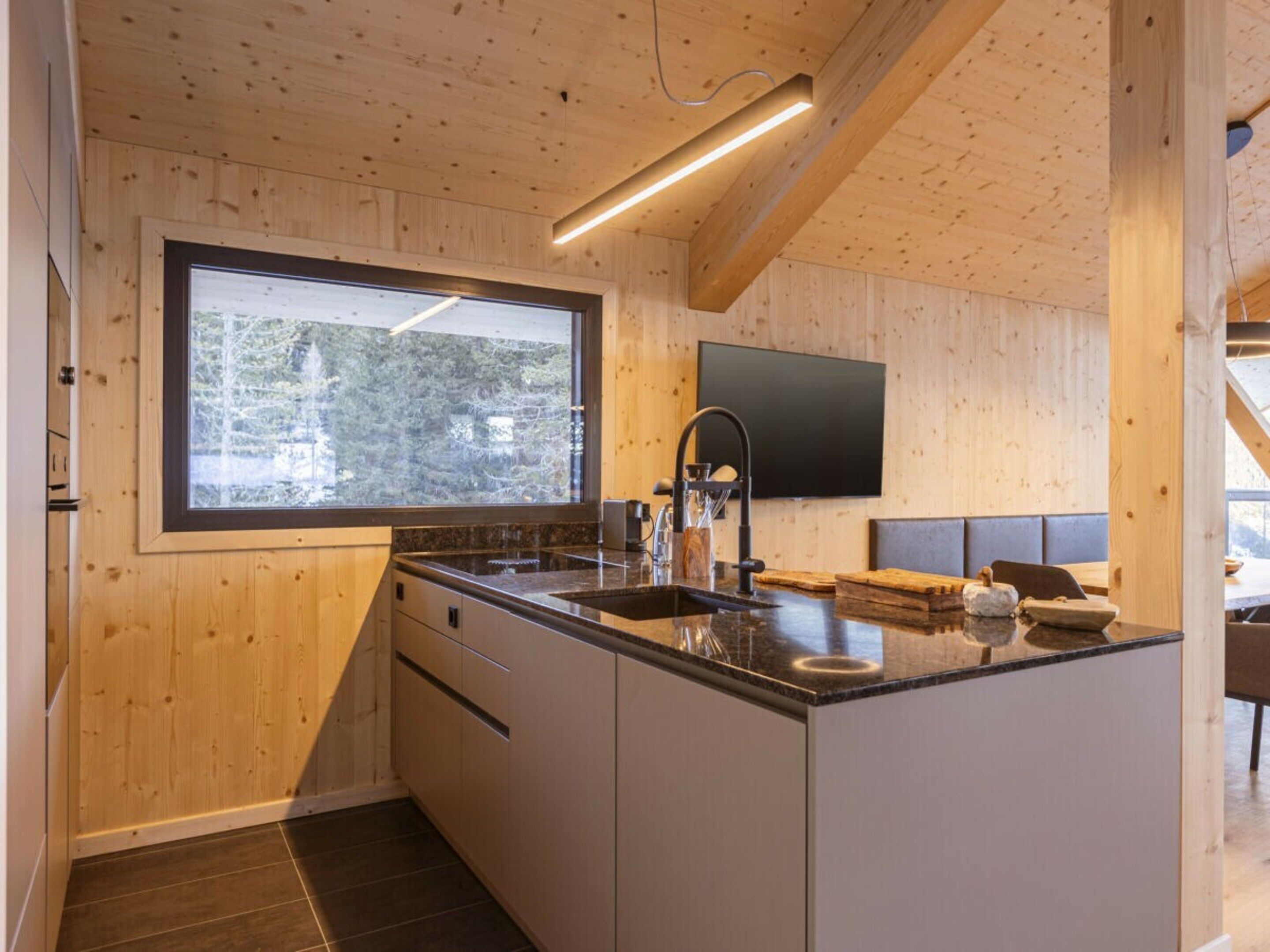 A modern kitchen with a large window, wooden walls, and a built-in island.