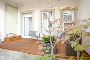 Eine Holzterrasse mit Gartenmöbeln, einem Blumentopf und einem Korbusch.