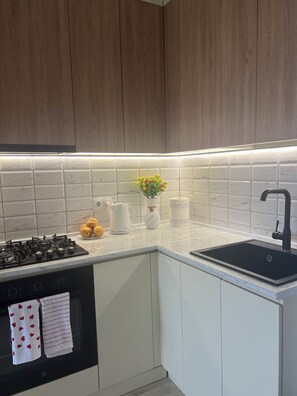 A modern kitchen with white cabinets, a black stove, a sink, and a vase with flowers on the countertop. - Bright & Cozy 2-Bedroom Apartment in Tbilisi, Just a 5-Minute Walk from the Metro (T'bilisi)