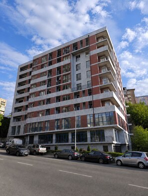 Un edificio residencial de varios pisos con balcones, ventanas amplias y un estacionamiento al frente.