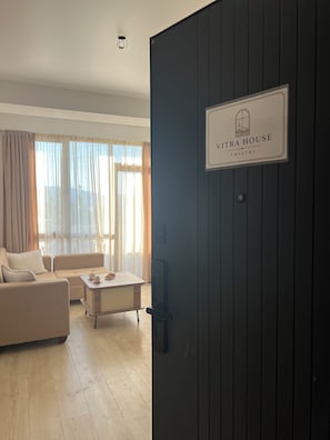 A modern living room with a sofa, a coffee table, and a TV. A sign on the wall reads 'VITRA HOUSE'. - Bright & Cozy 2-Bedroom Apartment in Tbilisi, Just a 5-Minute Walk from the Metro (T'bilisi)