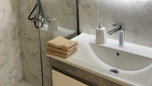 Une salle de bain dotée d’une douche à parois de verre, d’un lavabo blanc avec un robinet moderne et d’un grand miroir éclairé par un système d’éclairage circulaire.