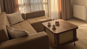 Un salon moderne avec un canapé d’angle, une table basse en bois et des rideaux en tissu léger.