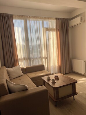 Una sala de estar moderna con un sofá seccional, una mesa de centro de madera y cortinas de gasa.