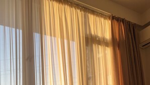 Una habitación con un ventanal grande cubierto por cortinas translúcidas, un sofá y un equipo de aire acondicionado.