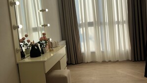 Une chambre d’hôtel avec une coiffeuse, un miroir avec éclairage, une plante en pot et une fenêtre avec des rideaux.