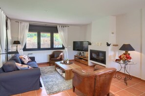 A living room with a sofa, armchair, coffee table, TV, fireplace, and a small table with a lamp. - Villa Helma in Begur (Begur)