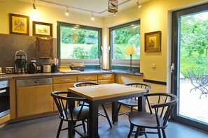 A kitchen with a dining table and chairs, a coffee machine, and a window with a view of greenery. - Henriette's holiday home (Bad Harzburg)