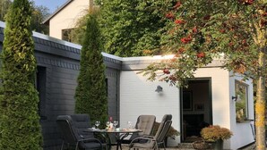 An outdoor seating area with a table and chairs, surrounded by greenery and a building. - Henriette's holiday home (Bad Harzburg)