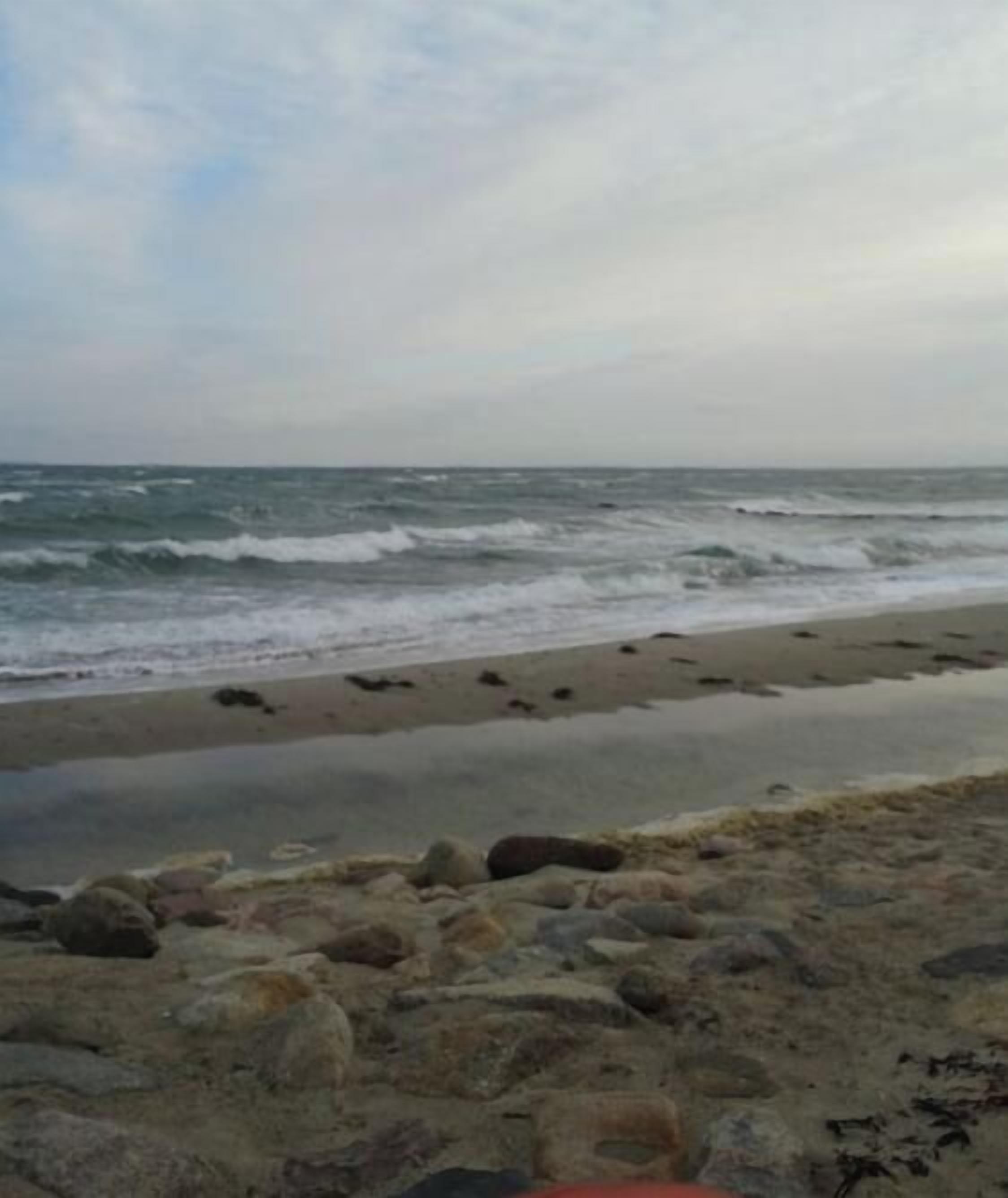 Une plage avec des vagues, des galets et un ciel nuageux.