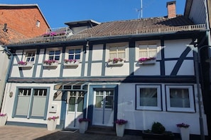 A traditional two-story building with a white facade and dark trim, featuring multiple windows with flower boxes and a visible door. - Holiday home with 2 bedrooms (Bodenwerder)