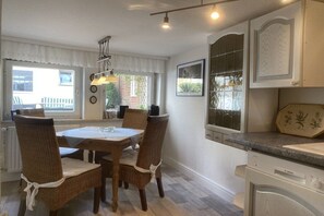 A dining area with a table and chairs, a window with curtains, and a kitchen area with cabinets and a Bosch dishwasher. - Holiday home with 2 bedrooms (Bodenwerder)