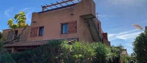 Un edificio con techo inclinado, una pérgola de madera en el nivel superior y un pequeño ventanal en la planta baja.