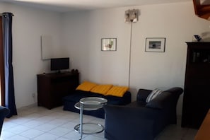 Ein Wohnzimmer mit einer Couch, einem kleinen runden Tisch, einem Fernseher und einem Schrank.