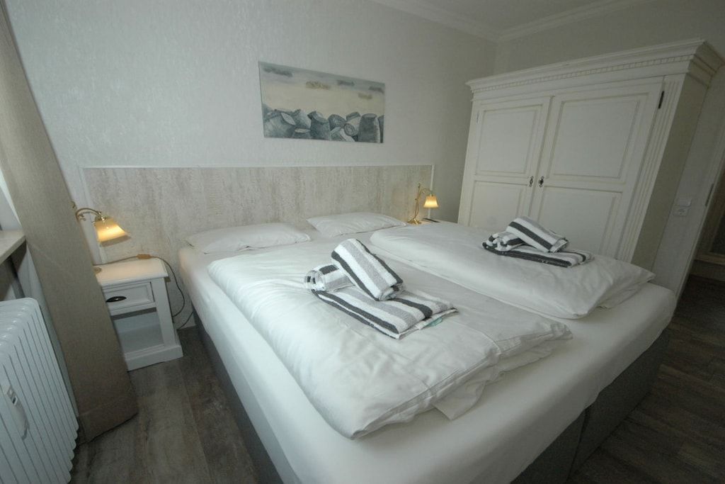 Une chambre d’hôtel avec un lit double, deux tables de chevet, une commode, un radiateur et une armoire.