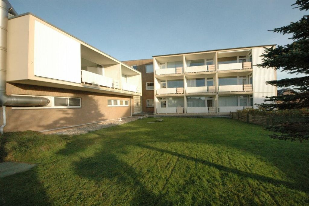 A modern multi-story residential building with balconies and a well-maintained lawn.