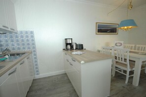 A compact kitchen with a sink, a coffee maker, and a dining area with chairs and a table. - Holiday apartment in Sylt with 1 bedroom (Wenningstedt)