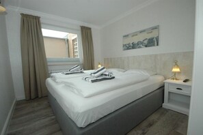 A hotel room with a double bed, a bedside table with a lamp, and a window with curtains. - Holiday apartment in Sylt with 1 bedroom (Wenningstedt)