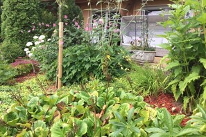 Un jardín con diversas plantas y flores, un enrejado de madera y una planta en maceta sobre un alféizar de ladrillo.