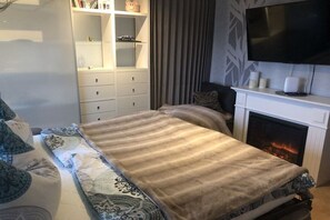 A bedroom with a bed, a television mounted on the wall, a fireplace, and a bookshelf. - Holiday apartment in the Harz Mountains with 1 bedroom (Blankenburg)
