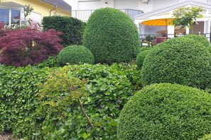 Un jardin bien entretenu, agrémenté de haies de différentes formes, avec un bâtiment jaune en arrière-plan.
