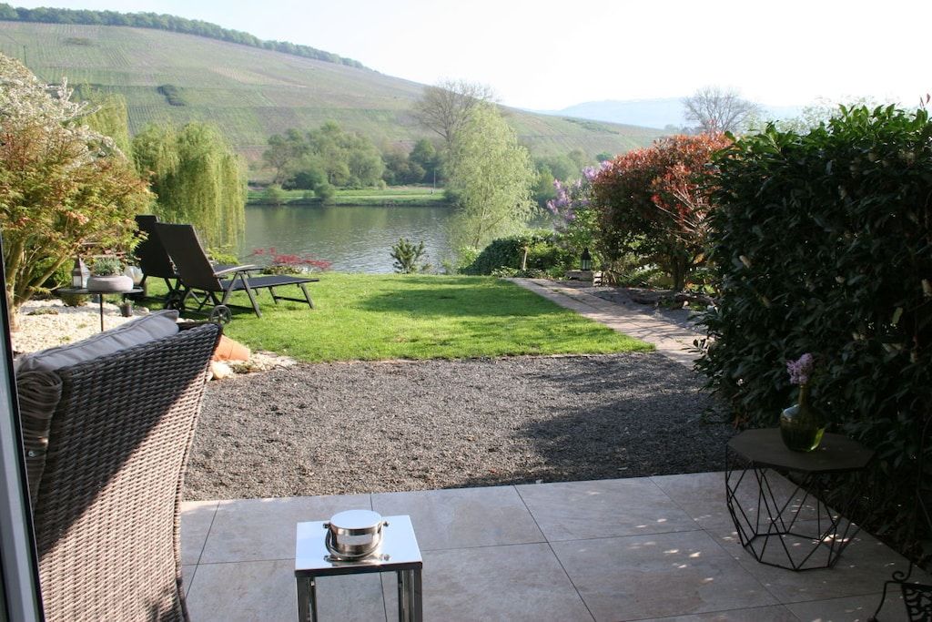 A patio with outdoor furniture, a table, and a view of a lake and hills.