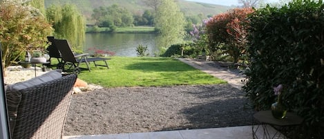 A patio with outdoor furniture, a table, and a view of a lake and hills.