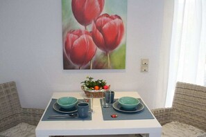 A dining area with a white table set for two, a basket of fruit, and a painting of red tulips on the wall. - "Abundance" on the banks of the Moselle (Bernkastel-Kues\/Andel)