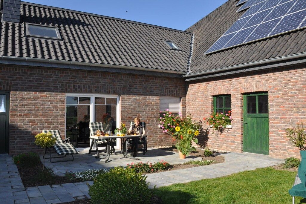 Een bakstenen huis met een pannendak, een terras met tuinmeubilair en zonnepanelen op het dak.