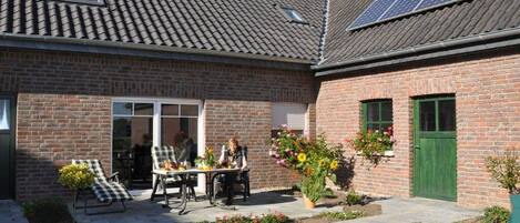 Een bakstenen huis met een pannendak, een terras met tuinmeubilair en zonnepanelen op het dak.