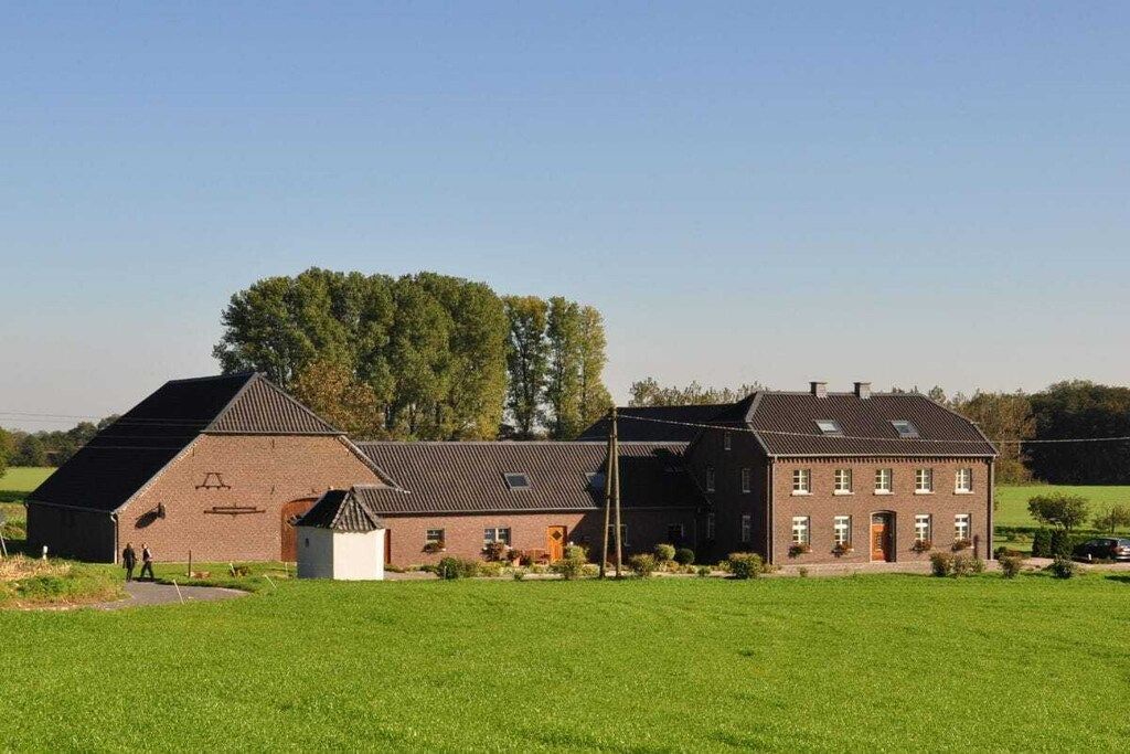 Une ferme avec une grande grange et une maison principale, entourée d’un champ verdoyant et d’arbres.