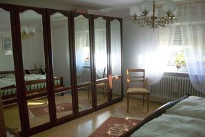 A bedroom with a large mirror, a wooden bed, a chair, and a radiator. - Holiday apartment with 1 bedroom (Impflingen)