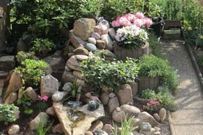 Um jardim com um pequeno lago rodeado por pedras e plantas.