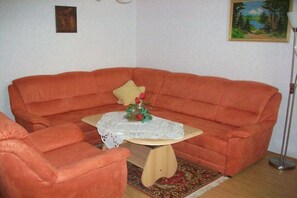 Uma sala de estar com sofá, uma mesinha com toalha de renda e uma poltrona.