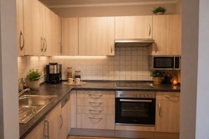 A modern kitchen with wooden cabinets, a stainless steel sink, a built-in oven, and a microwave. - at the Stark holiday farm (Kelheim)