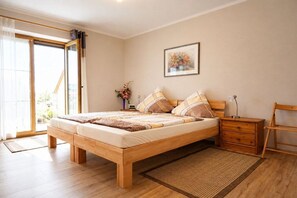 A bedroom with a wooden bed, a nightstand, a chair, a window with curtains, and a painting on the wall.