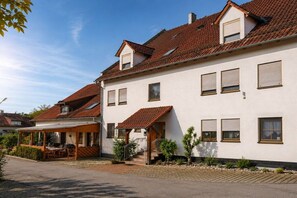 A two-story residential building with a tiled roof, a covered patio, and a small garden area. - at the Stark holiday farm (Kelheim)