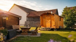 Une cabane en bois avec une véranda, une table et des chaises, située dans une cour arrière entourée d’une clôture et agrémentée d’un arbre.