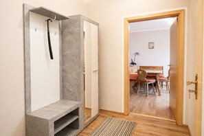 A hallway with a shower area, a wooden door leading to a dining area with a table and chairs.