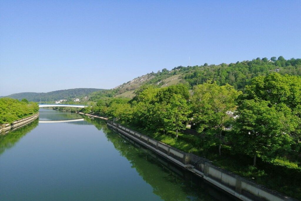 Ein Fluss mit einer Brücke und einem bewaldeten Hügelhang.