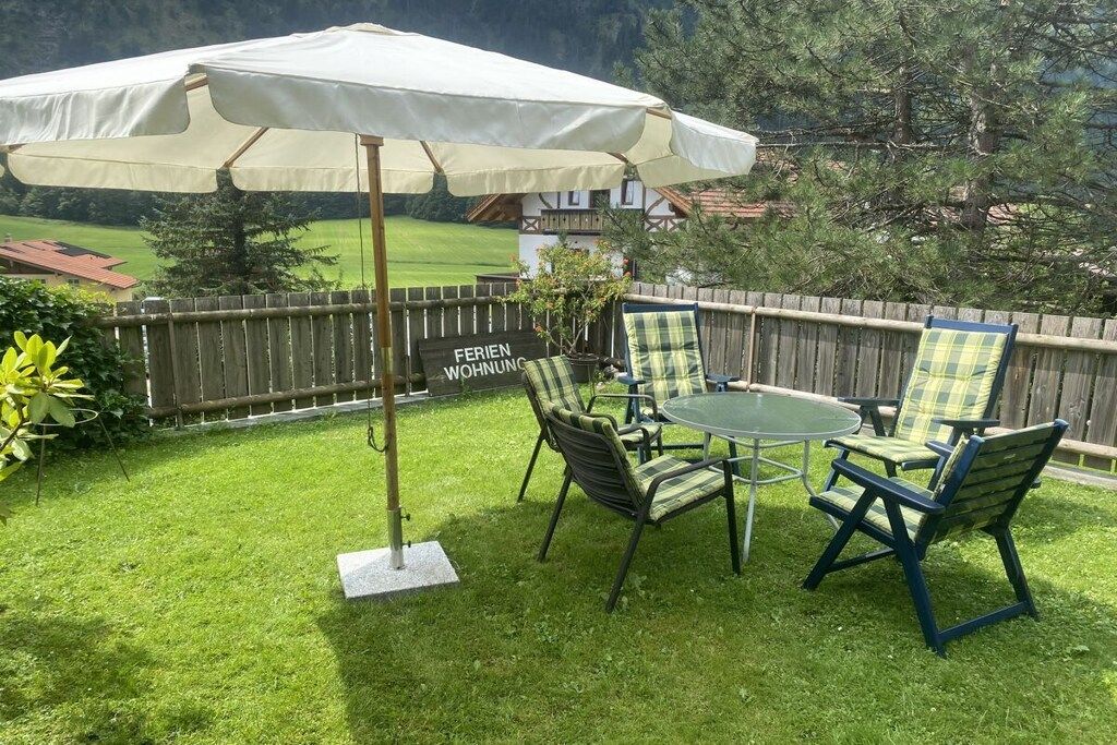 A patio with a table and chairs, a white umbrella, and a sign that reads 'FERIEN WOHNUNG.'