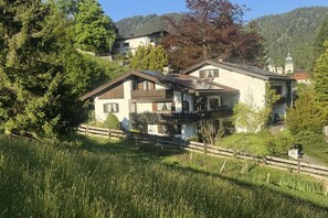 Ein traditionelles Chalet mit Balkon, umgeben von üppiger Vegetation und einer Bergkulisse.