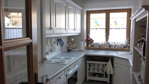 Une cuisine avec des meubles blancs, une fenêtre avec des rideaux et un plan de travail sur lequel se trouvent divers ustensiles de cuisine.